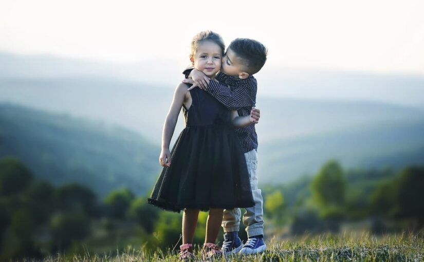 A boy kissing a girl on the cheek in a scenic outdoor setting