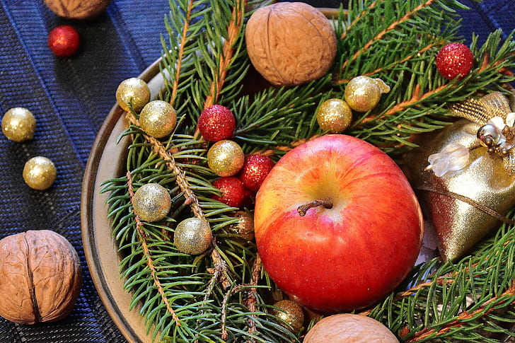 On a table covered with a blue tablecloth is a platter with pine branches and pinecones, Christmas decorations, walnuts and an apple
