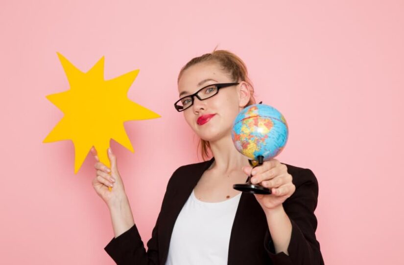 A woman holds a yellow starburst and a small globe against a pink background