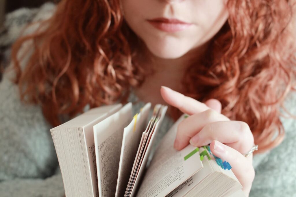 Red-haired female with a serious facial expression looking through a book