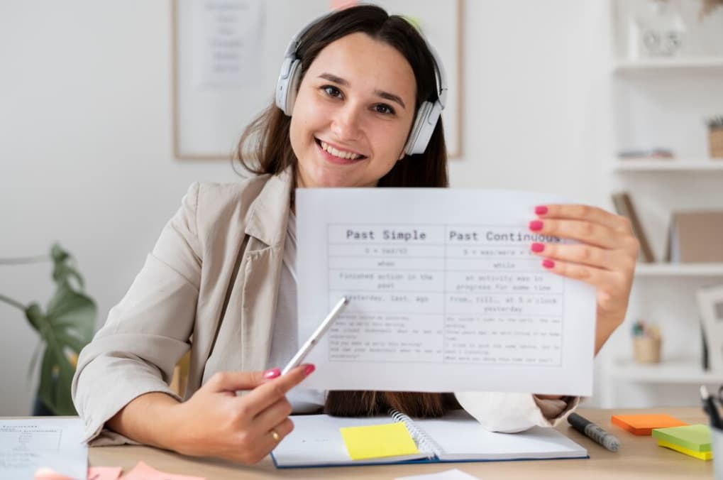 A smiling woman with headphones shows a grammar comparison chart