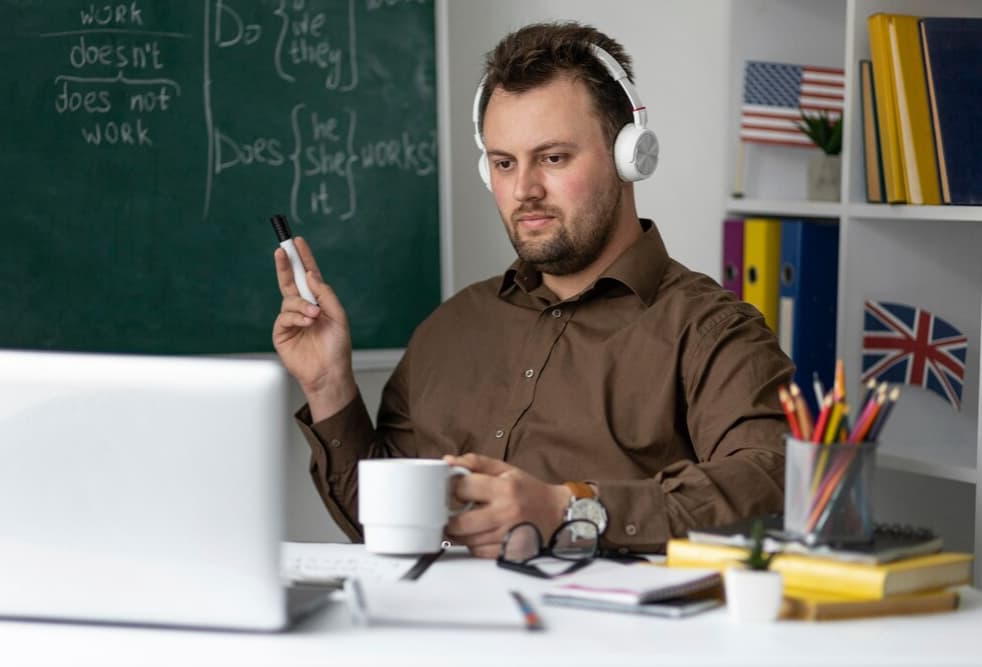 A focused man with headphones holds a pen, staring at a laptop